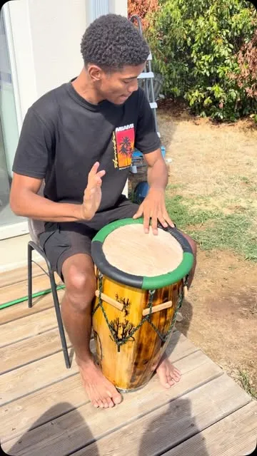 Un tanbouyé joue d'un ka jaune pyrogravé, assis en plein air